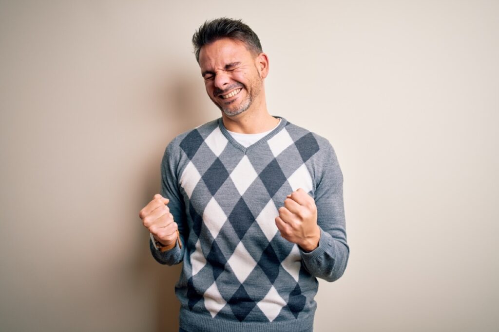 Young handsome man wearing casual sweater standing over isolated white background excited for success with arms raised and eyes closed celebrating victory smiling. Winner concept.