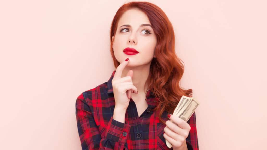 woman with money in red shirt - MassonShutterstock
